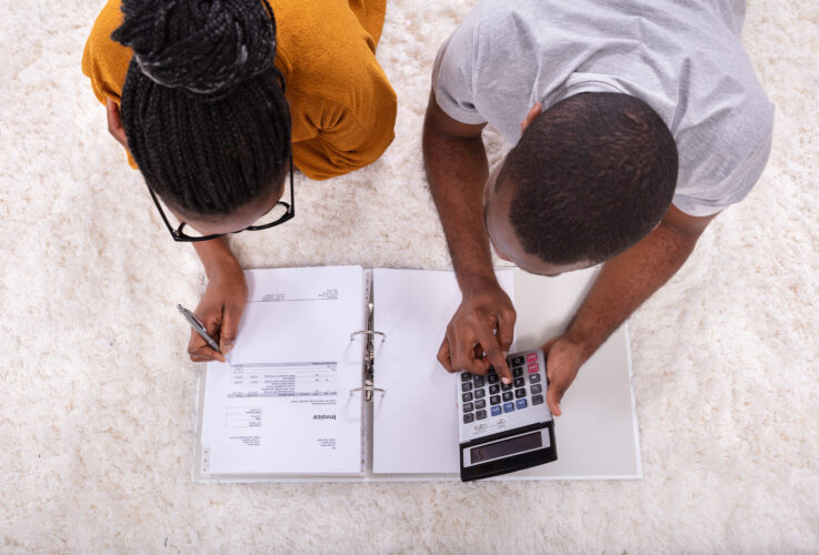 Young African Couple Lying On Carpet Invoice With Calculator